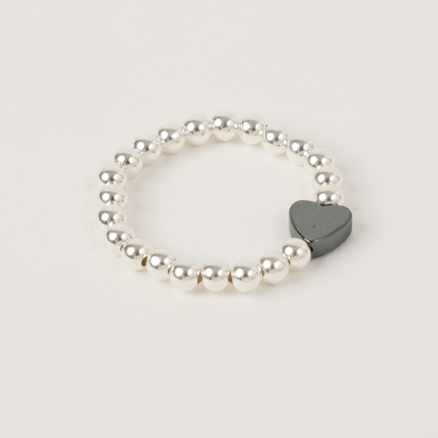 Pearl bracelet with a heart-shaped gray charm on a light gray background