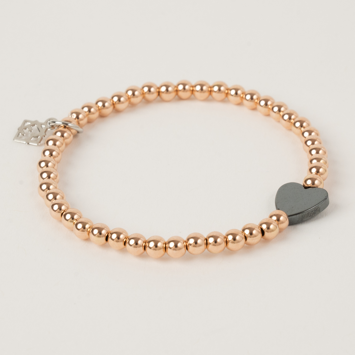 Rose gold beaded bracelet with a heart-shaped charm on a light gray background