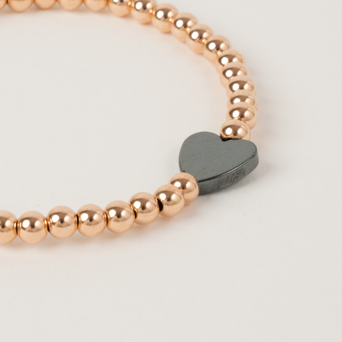 Rose gold beaded bracelet with a heart-shaped black tag on a light background