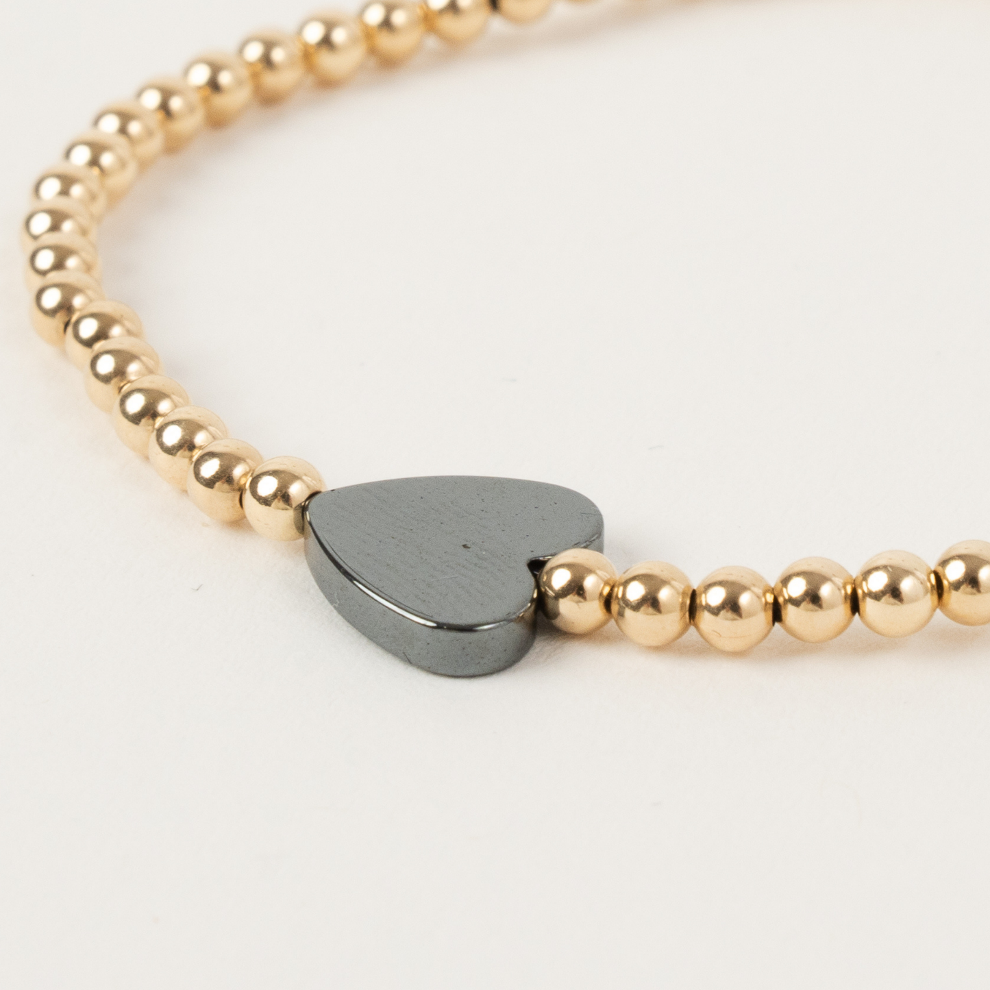 Gold beaded bracelet with a heart-shaped metal charm on a light background
