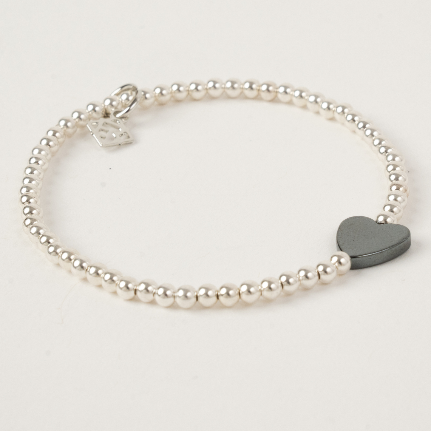 Pearl bracelet with a heart-shaped gray charm on a light gray background