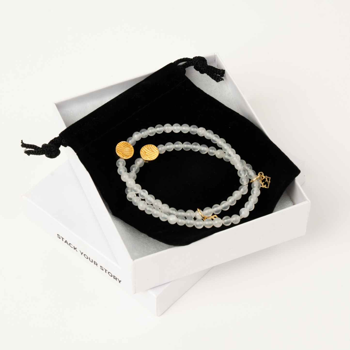 Beaded bracelet with gold accents on a black drawstring bag with 'Stack Your Story' branding.