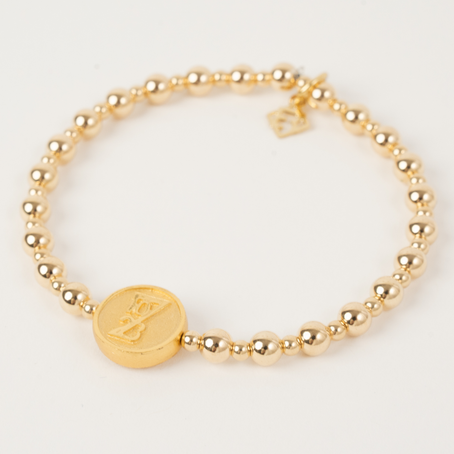 Gold beaded bracelet with a round gold charm on a light gray background