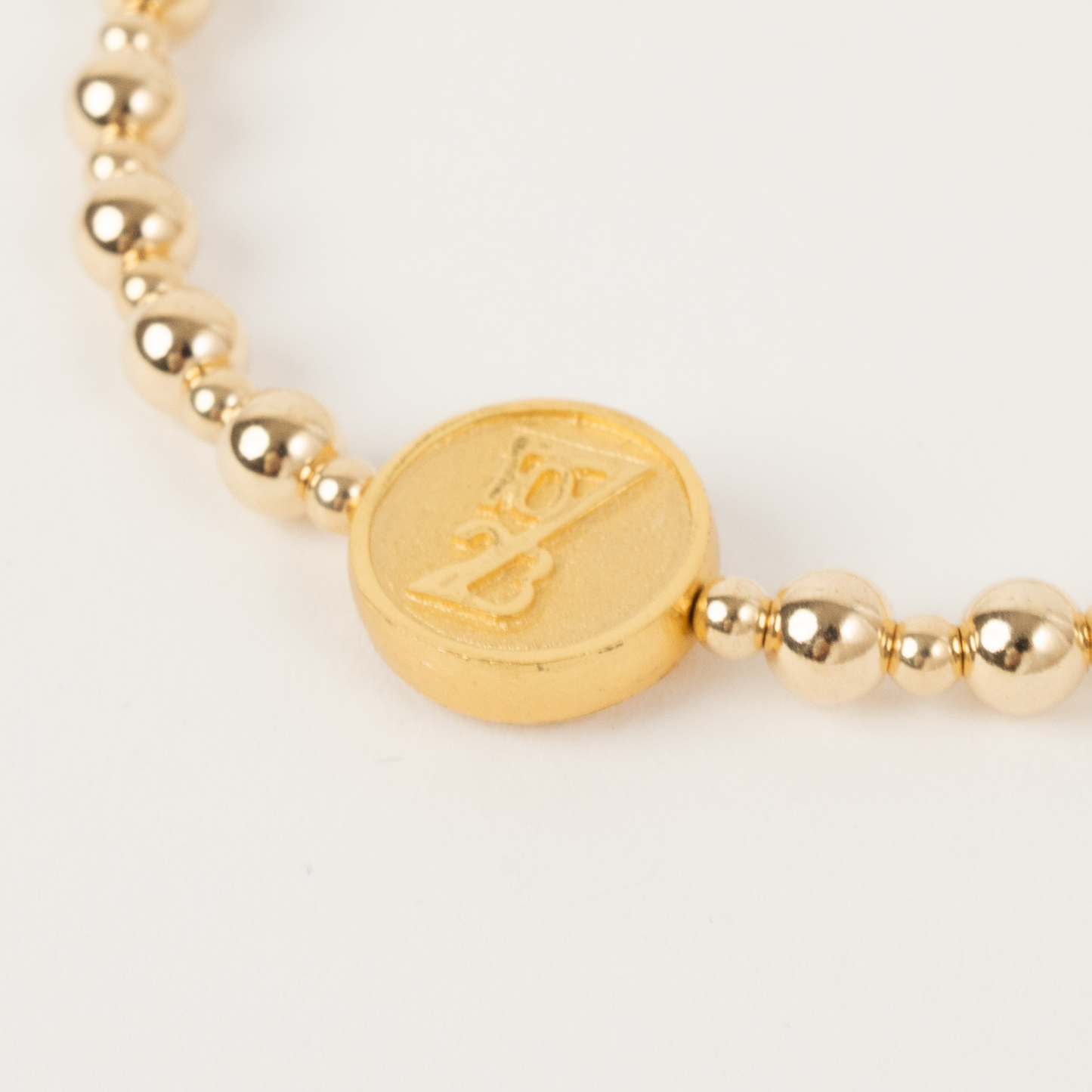 Gold beaded bracelet with a circular gold charm on a light gray background