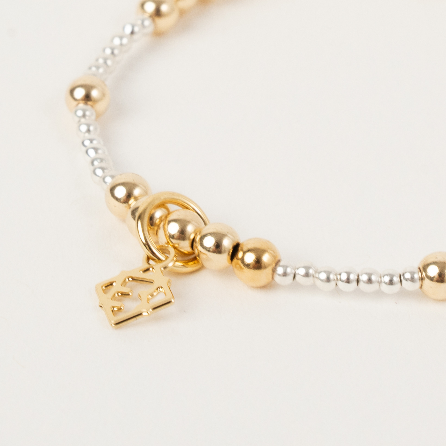 Gold and silver beaded bracelet with a heart charm on a light background
