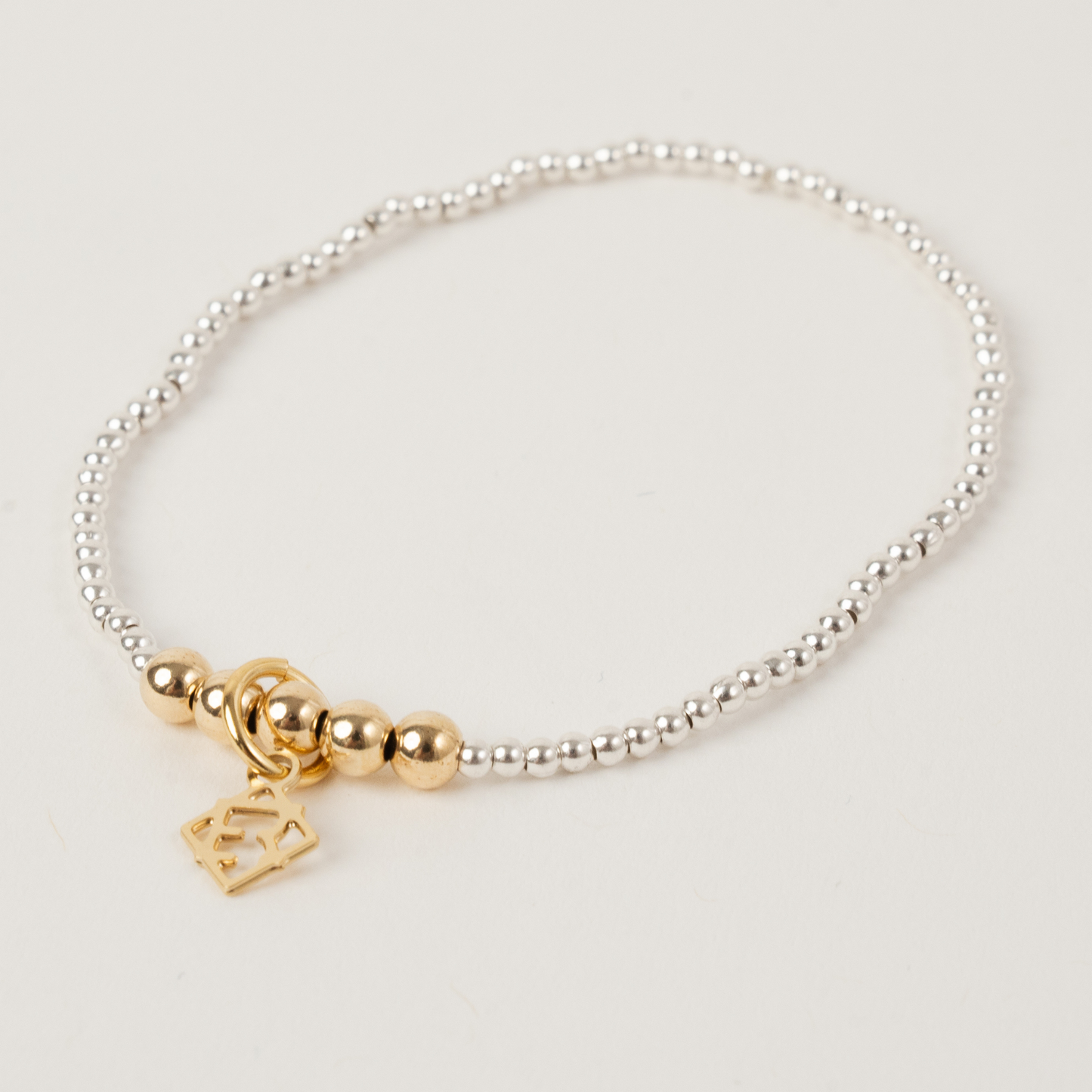 Silver bracelet with gold beads and a heart charm on a light gray background