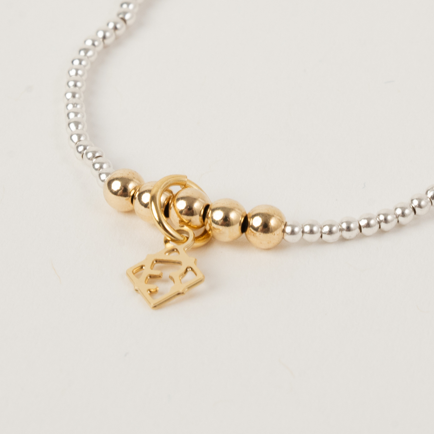 Gold beaded bracelet with a heart and star charm on a light background