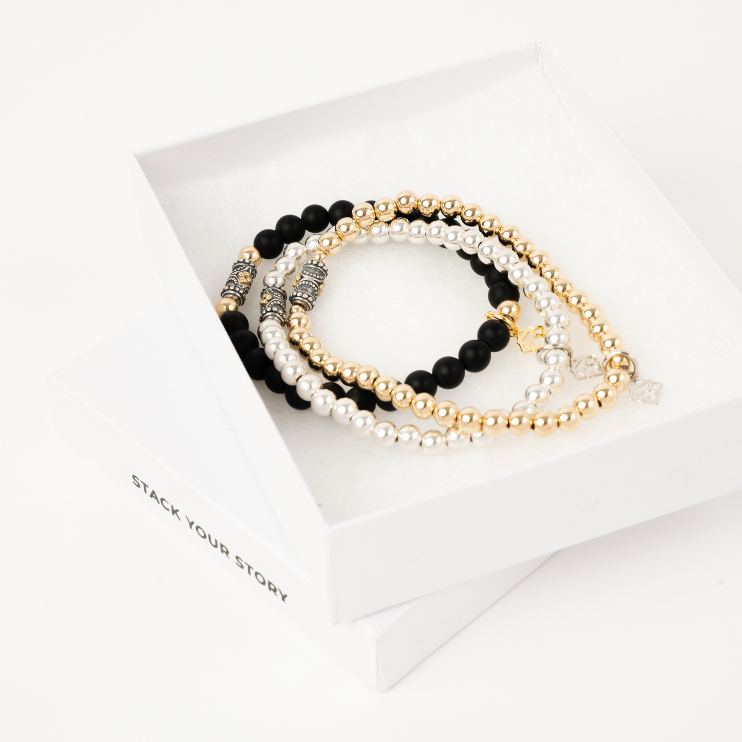 Set of pearl and black beaded bracelets on a white surface with 'Stack Your Story' branding.
