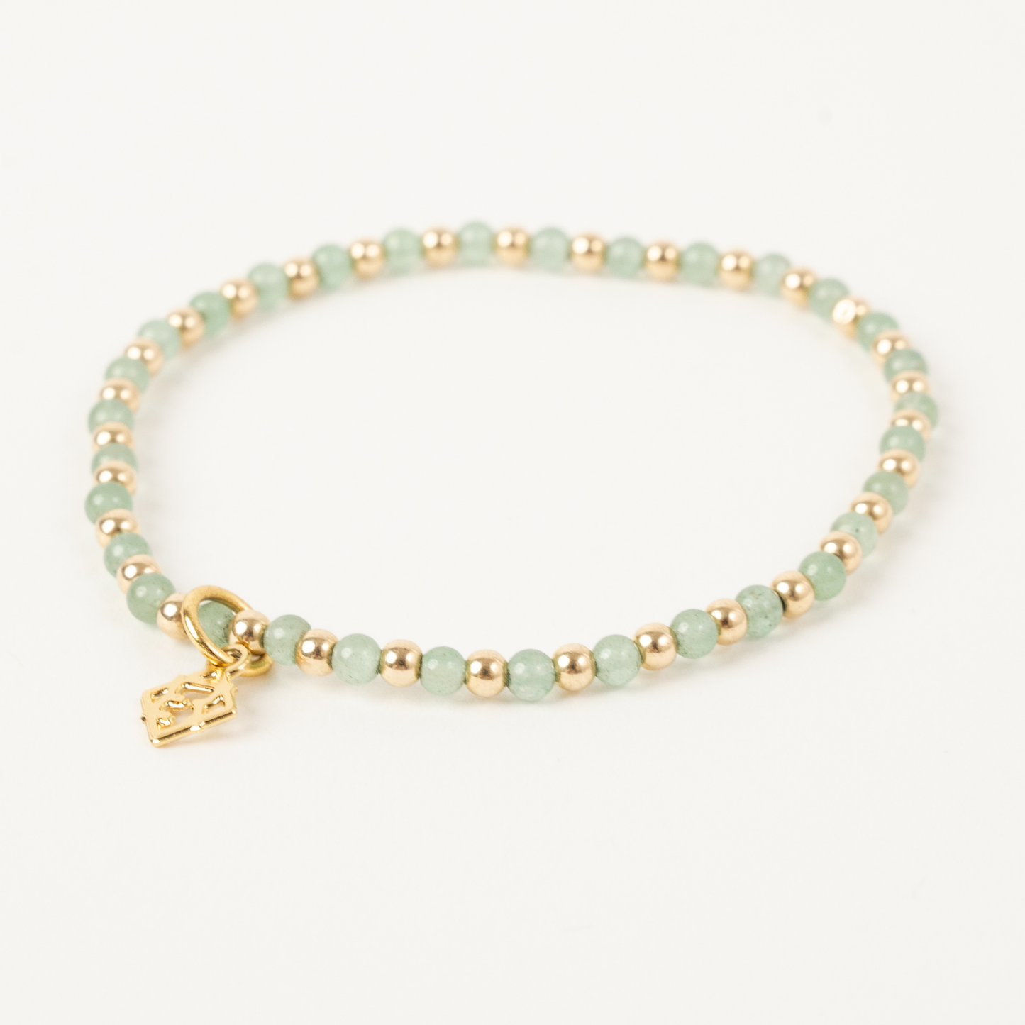 Bracelet with green beads and a gold charm on a white background