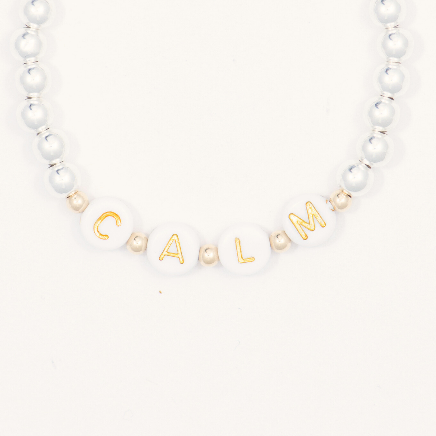 Bracelet with white beads and gold letter beads spelling 'CALM' on a white background