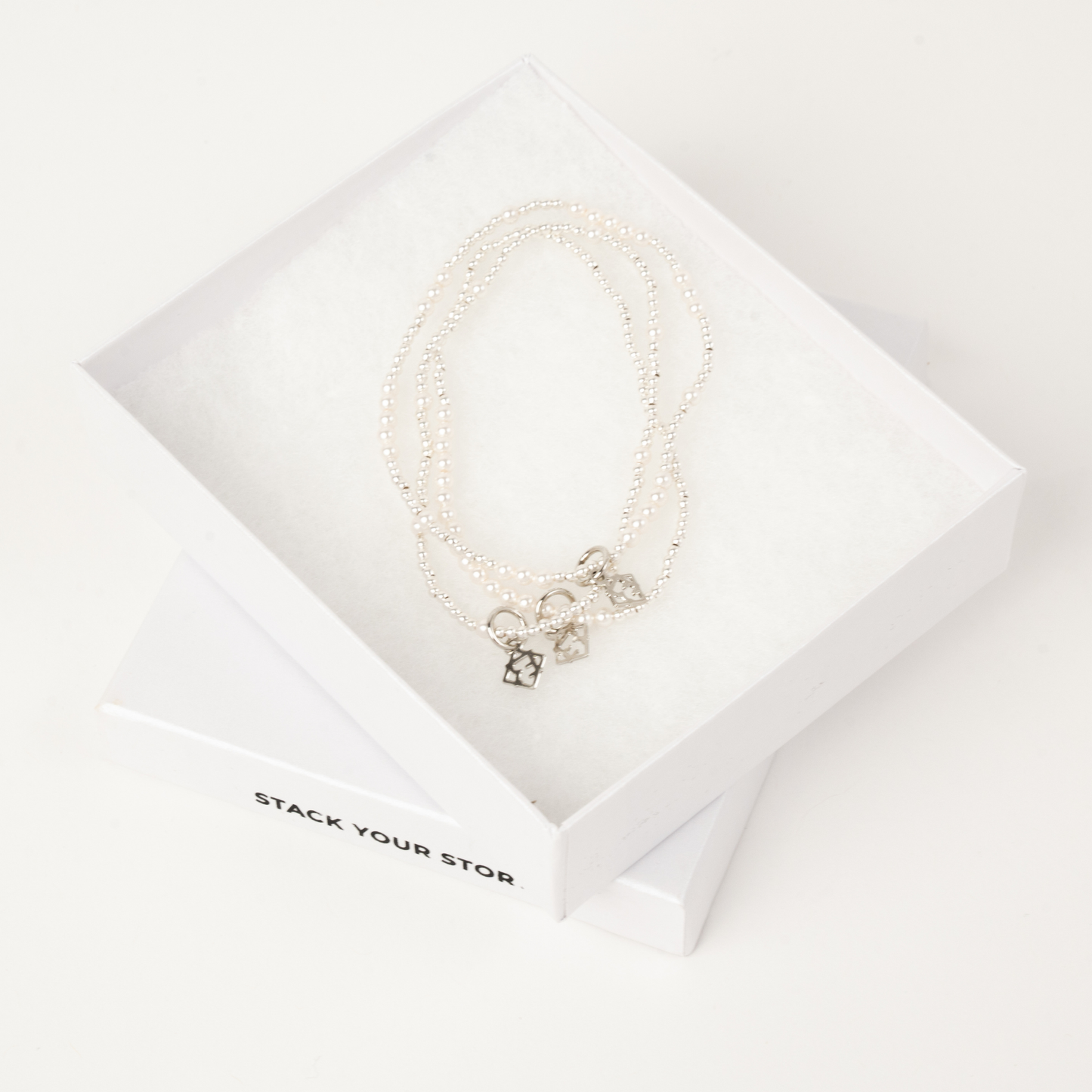 Pearl necklace with silver charms on a white card with 'STACK YOUR STORY' text.