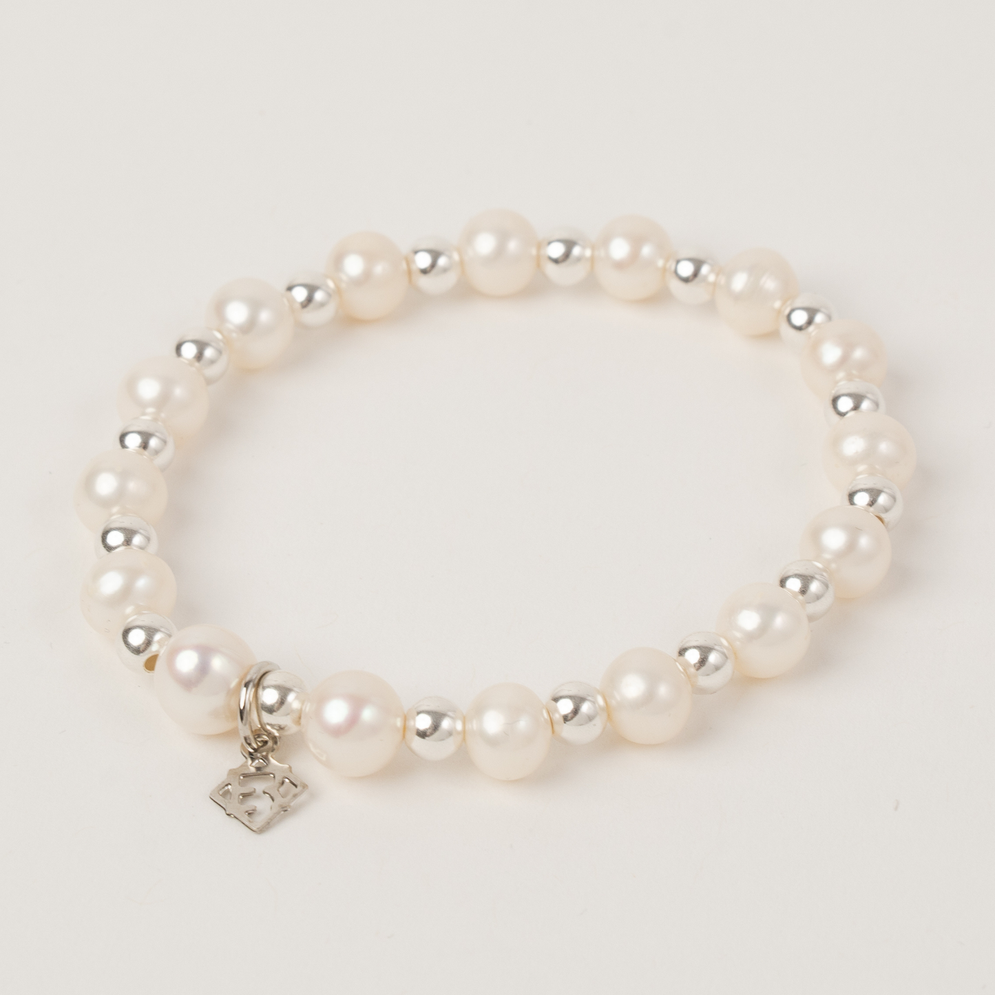 Pearl bracelet with silver charm on a light gray background