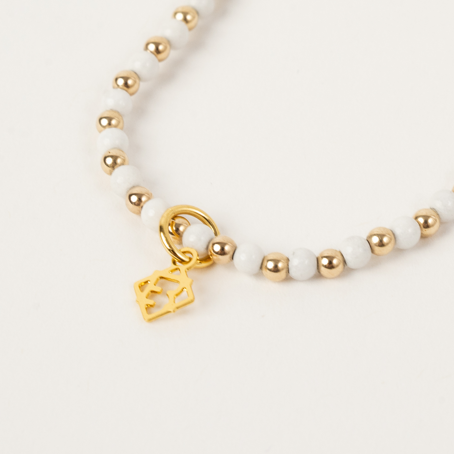 Bracelet with gold and white beads and a gold charm on a light background