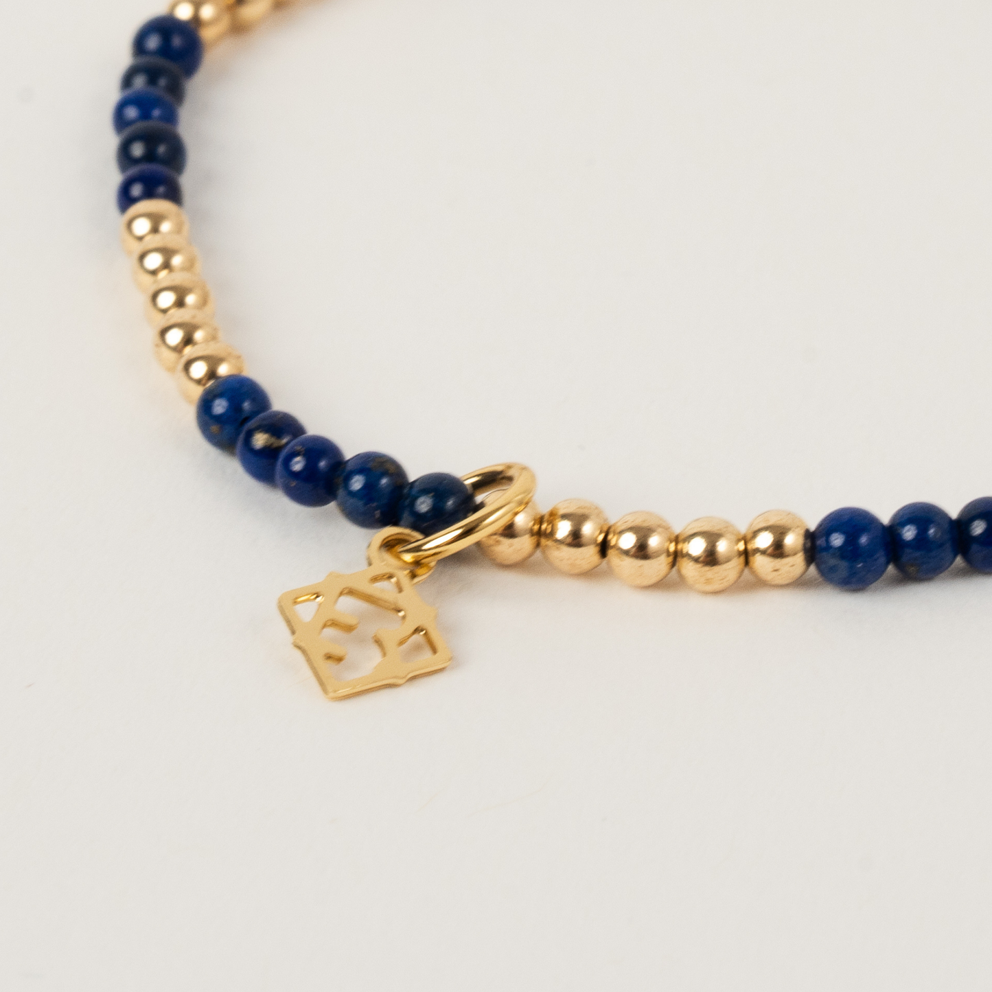 Bracelet with blue beads and gold charm on a light gray background