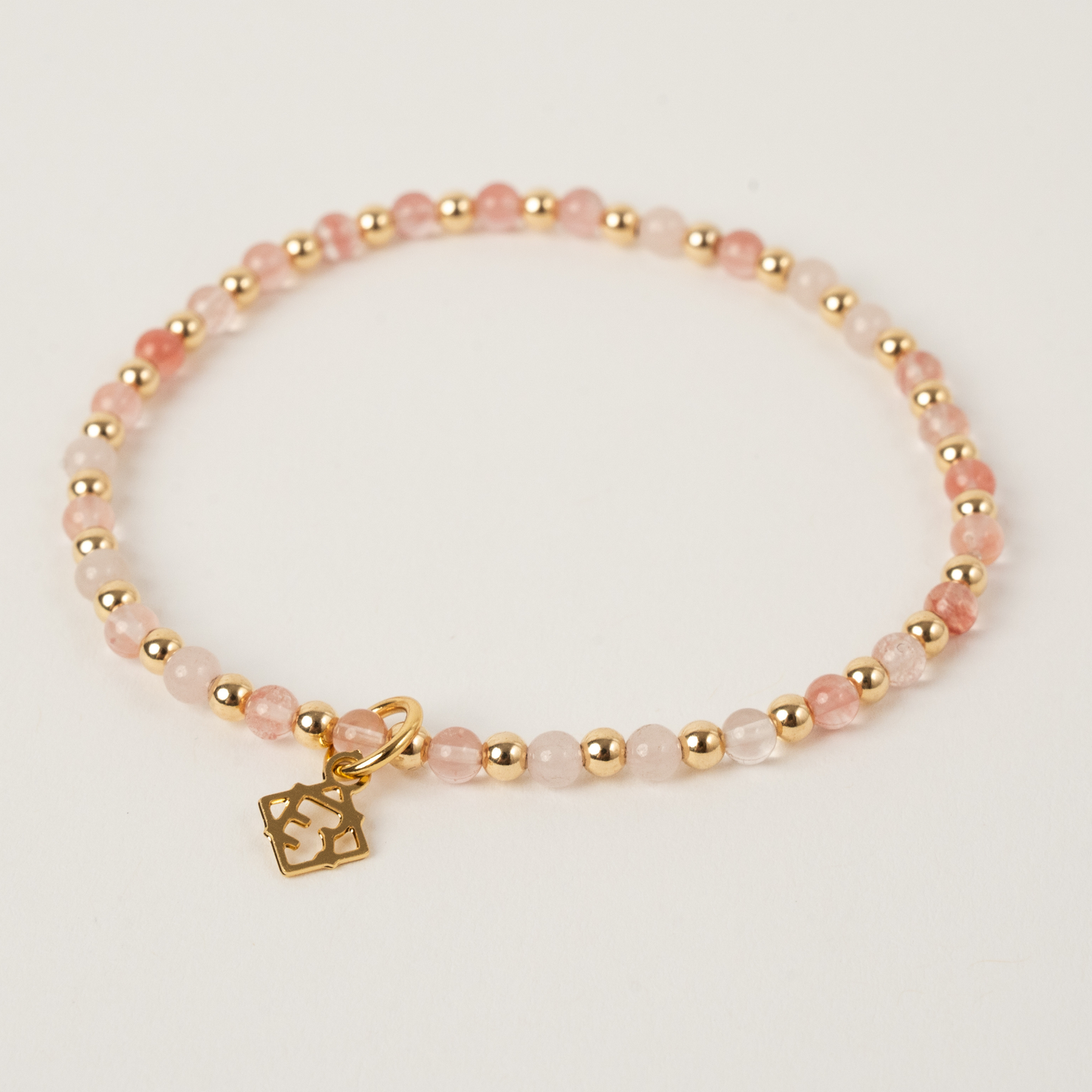 Bracelet with pink beads and gold charm on a light background