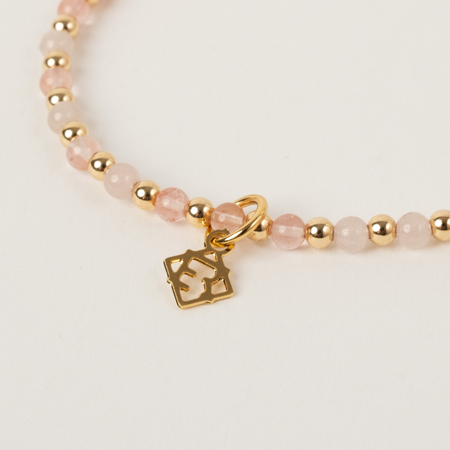 Bracelet with pink beads and gold charm on a light background