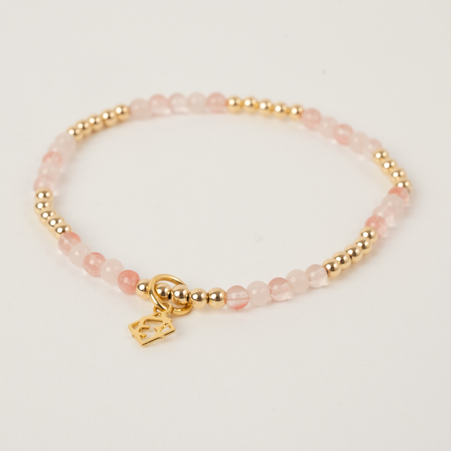 Bracelet with pink beads and gold charm on a light background