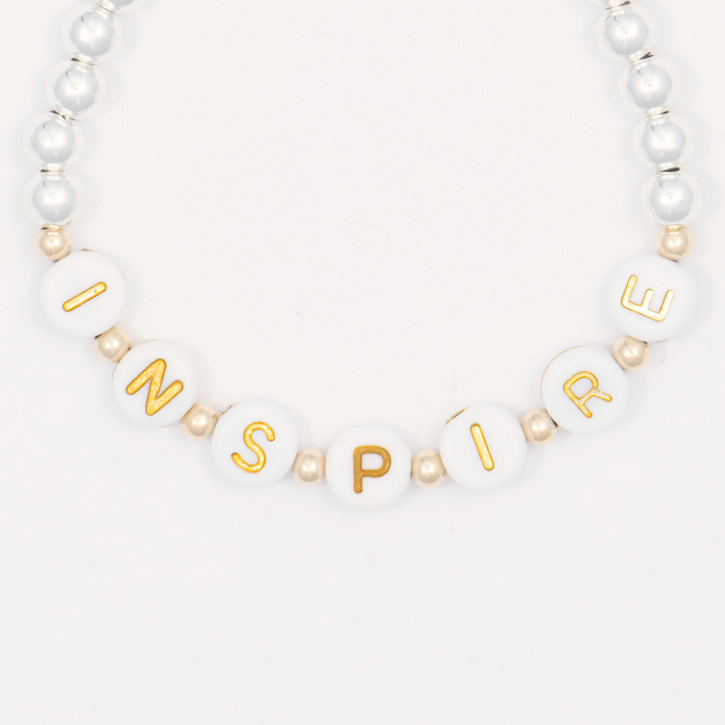 Bracelet with gold lettered beads spelling 'INSPIRE' on a white background