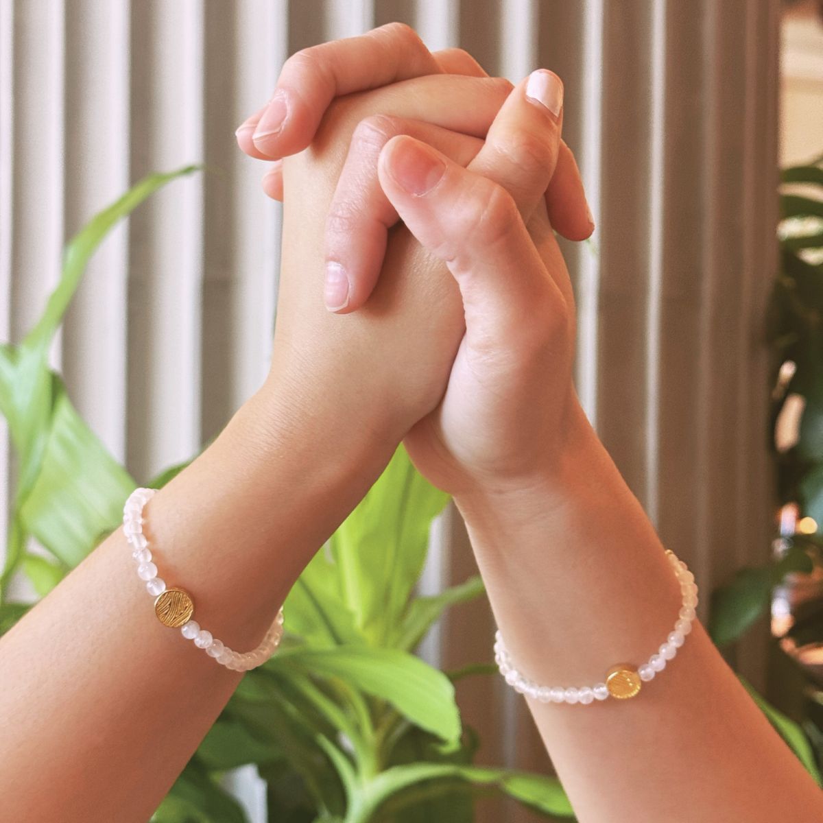 Woman holding hands wearing clear beaded bracelets with gold accent charms