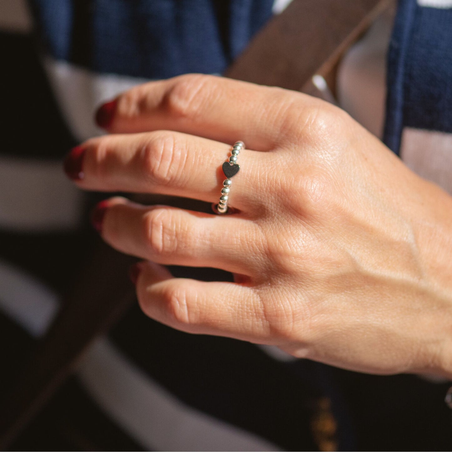 A person's hand showcasing a gold-filled micro ring with a heart-shaped hematite bead on the finger.