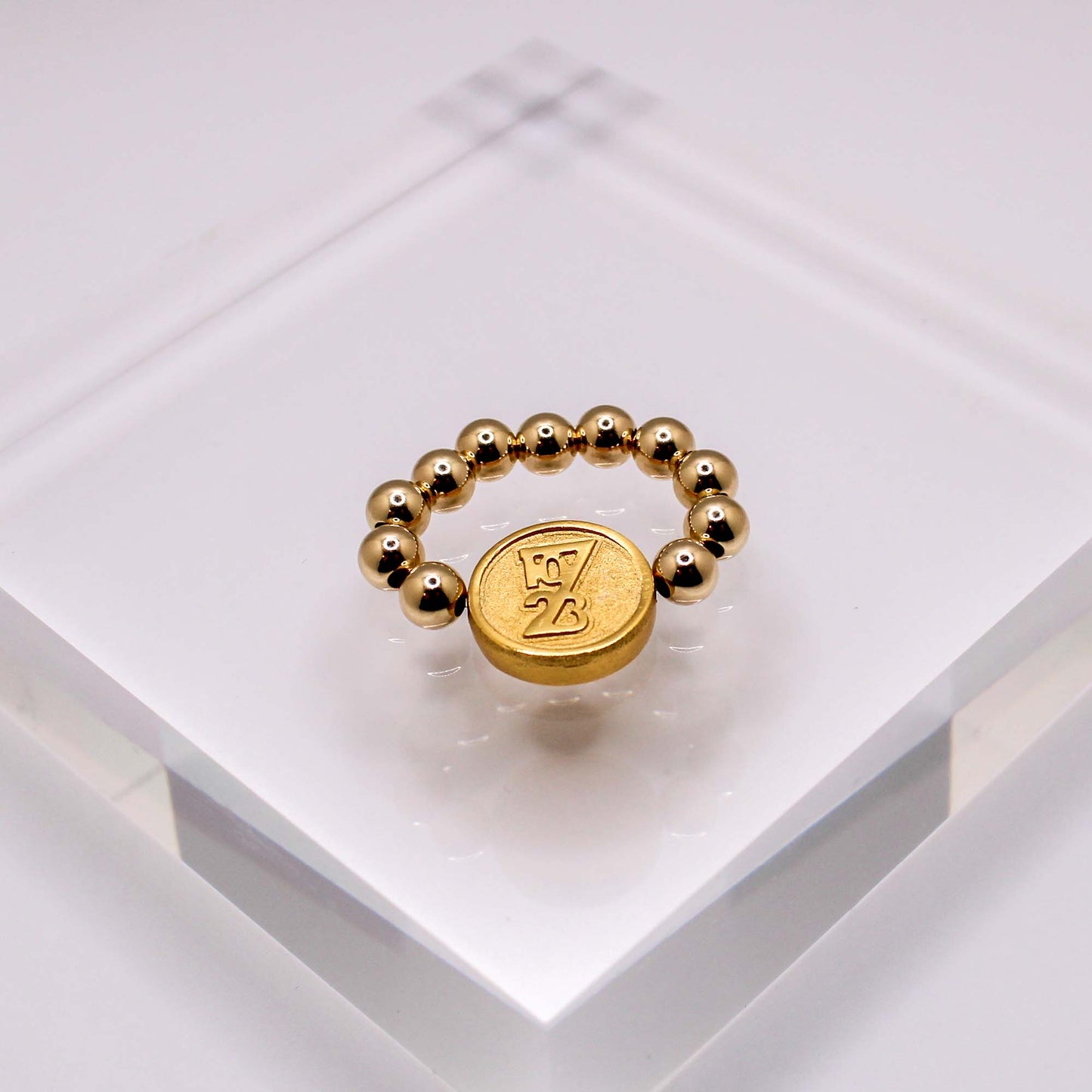 A gold-filled ring with abstract design, featuring a gold circular bead and gold or silver beads in between, displayed on a clear acrylic stand.