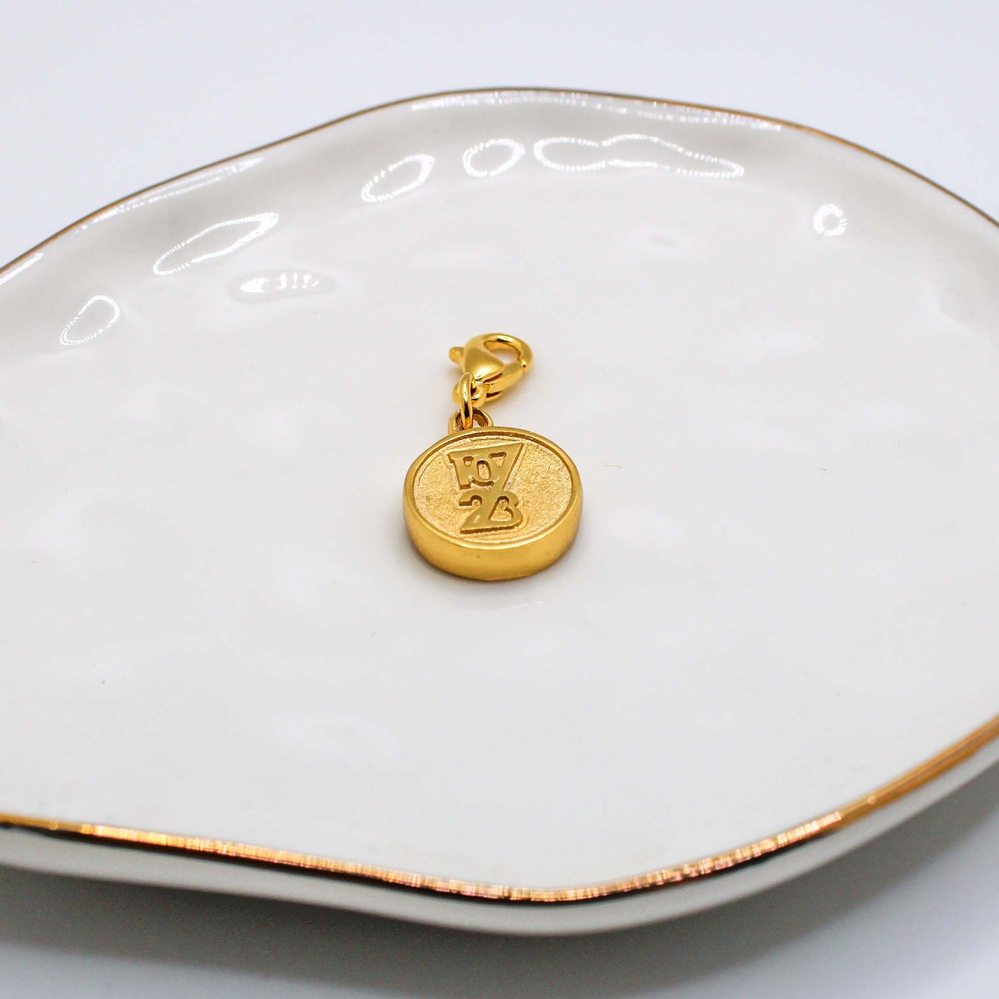 Two charity pendants on a white dish, one silver and one gold, each with a different design.