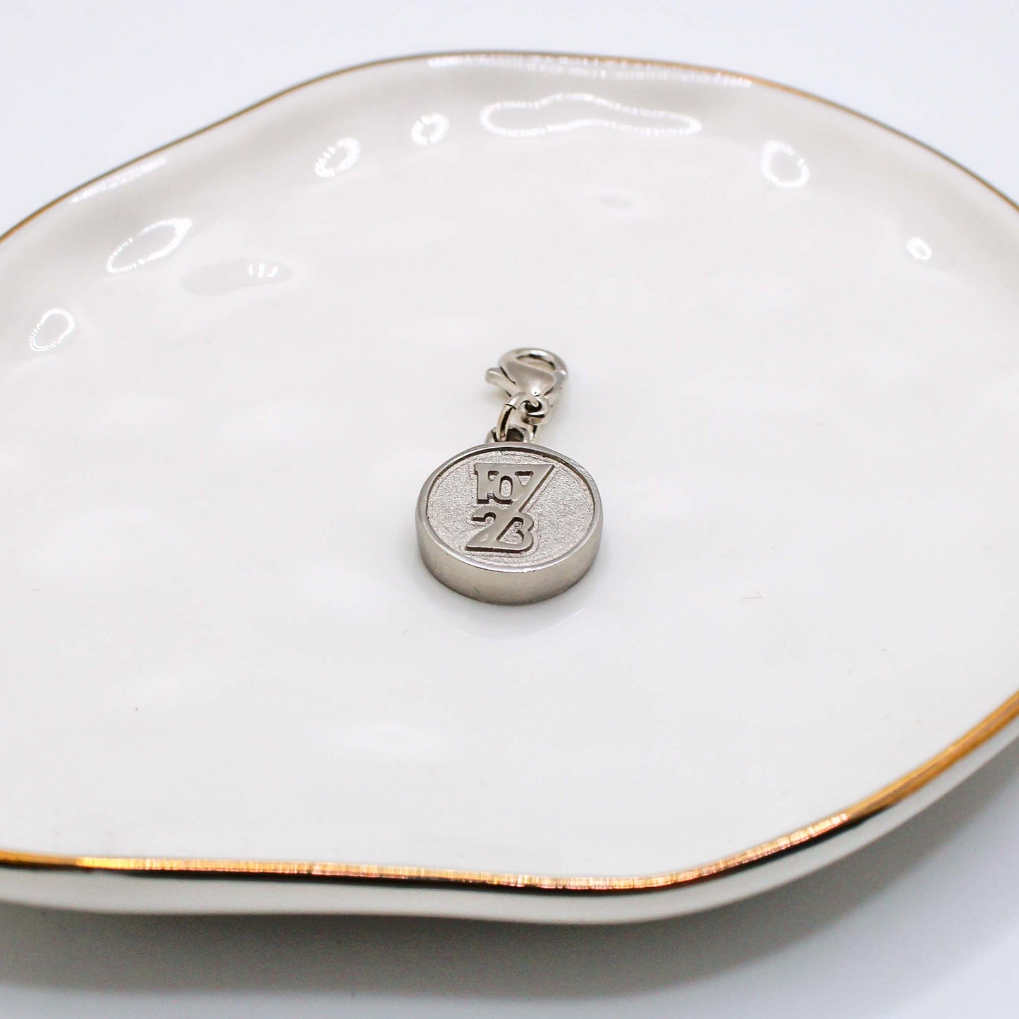 Two charity pendants on a white dish, one silver and one gold, each with a different design.
