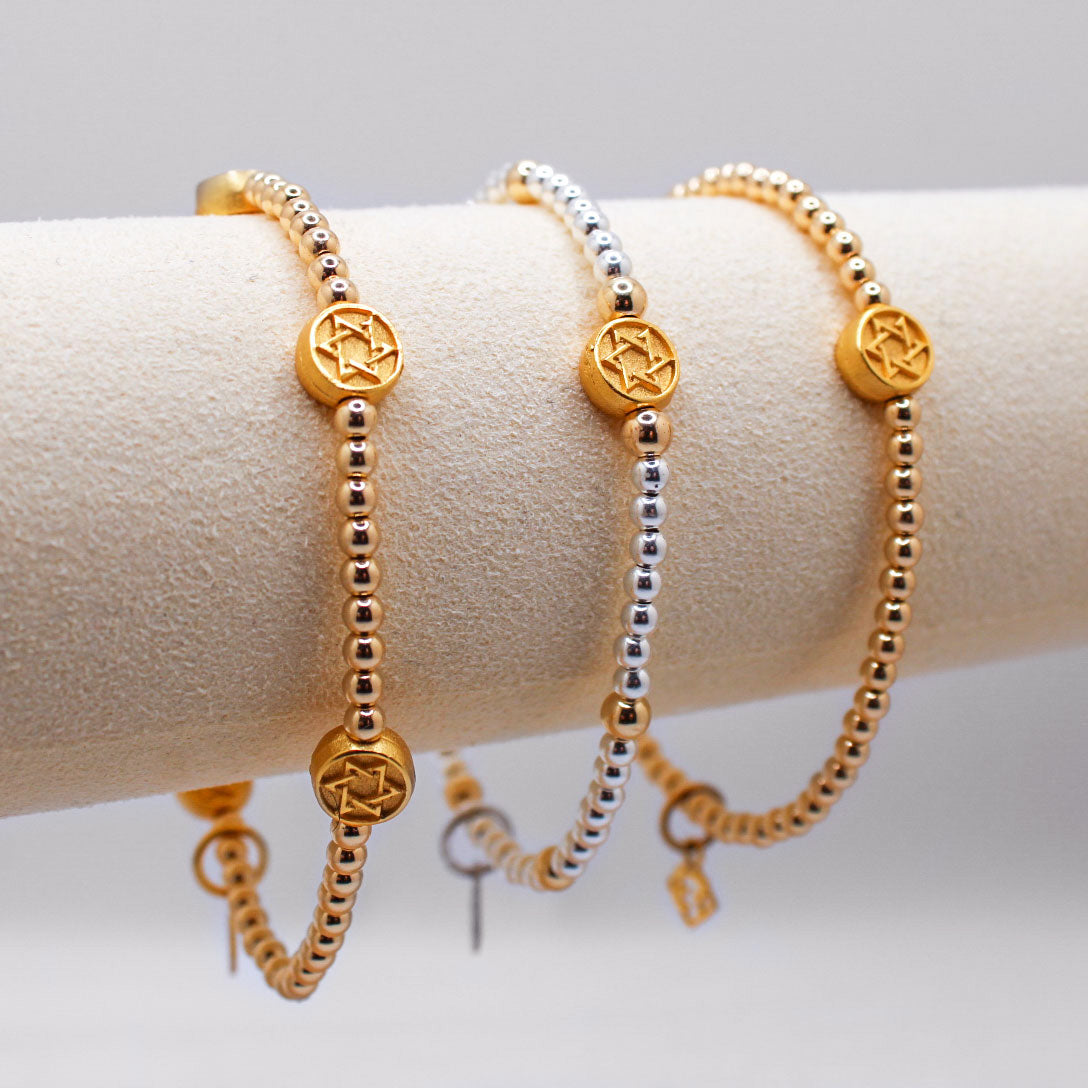 Three bracelets displayed on a wrist, featuring combinations of gold-filled and sterling silver beads along with golden stars.