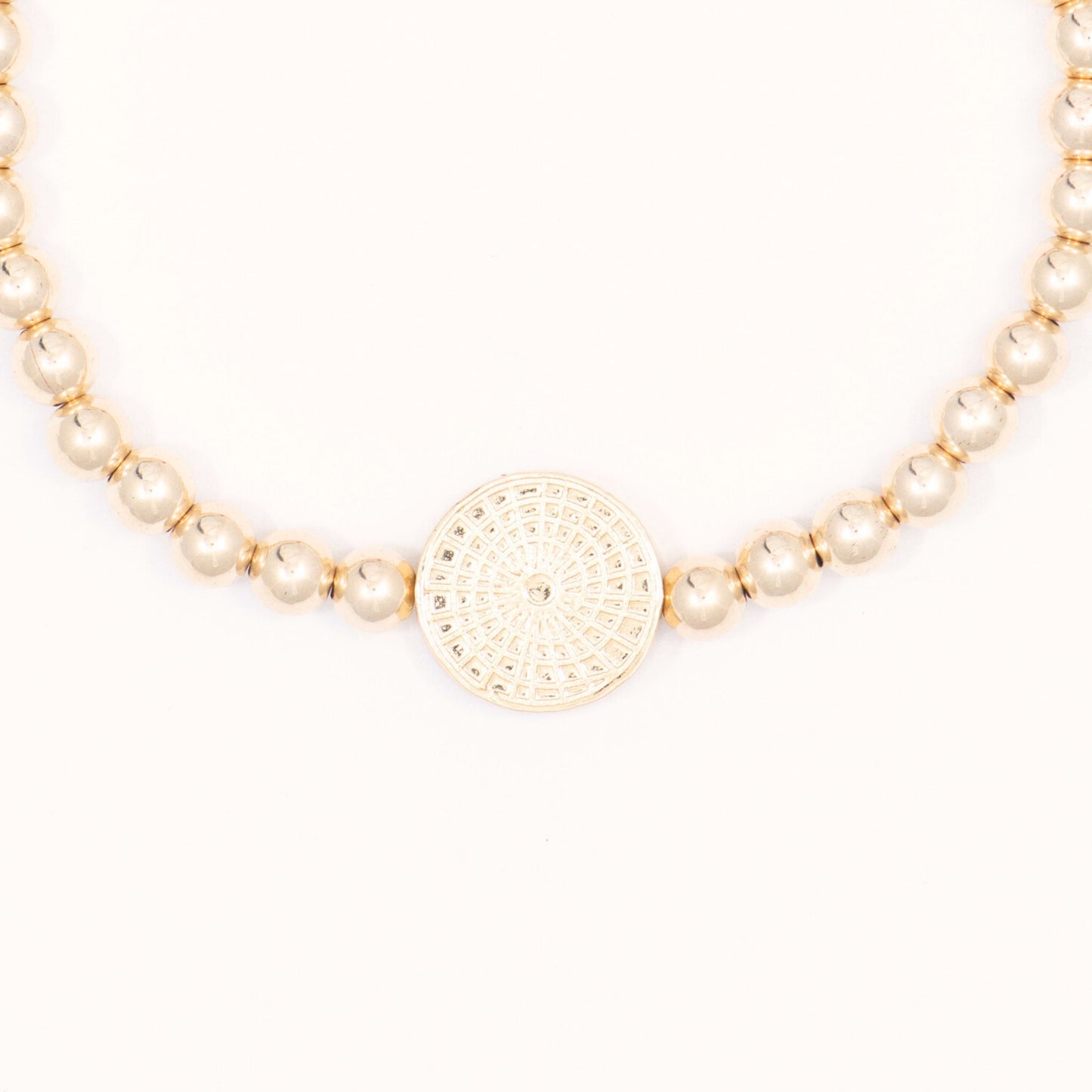 Gold beaded necklace with a round gold pendant on a white background