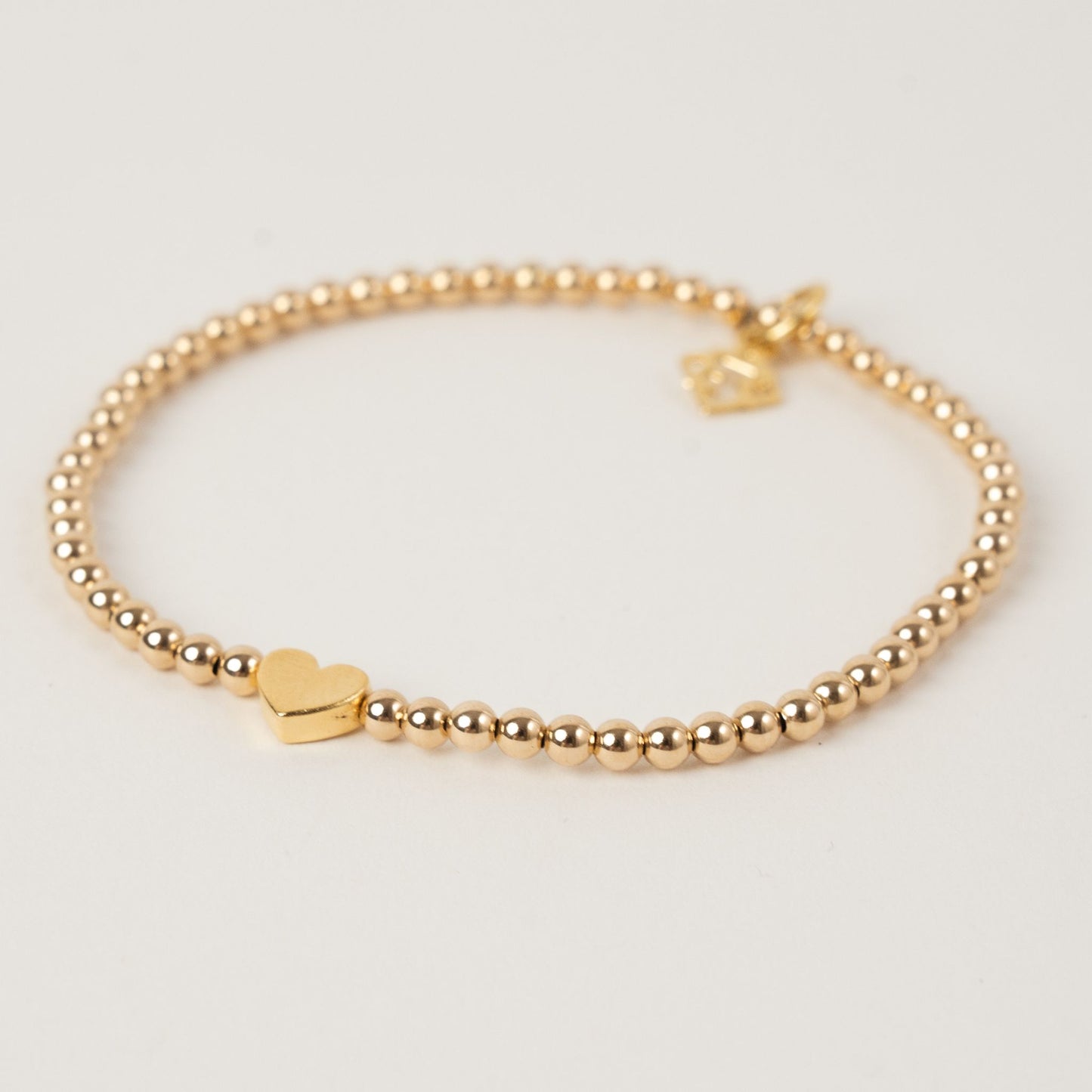 Gold beaded bracelet with a heart charm on a light gray background