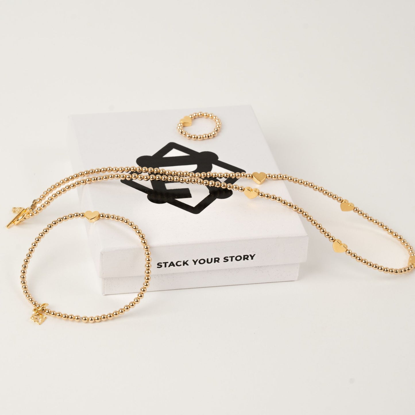 Gold bracelet, necklace, and ring on a white surface with 'Stack Your Story' text