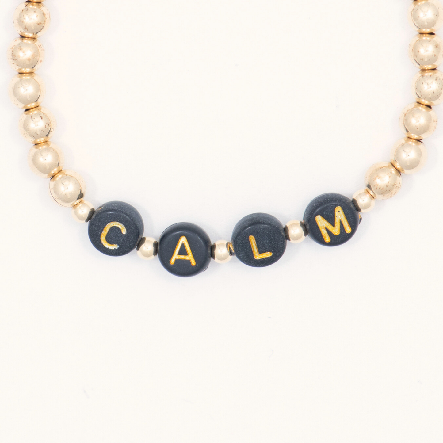 Bracelet with black beads featuring gold letters spelling 'CALM' on a white background