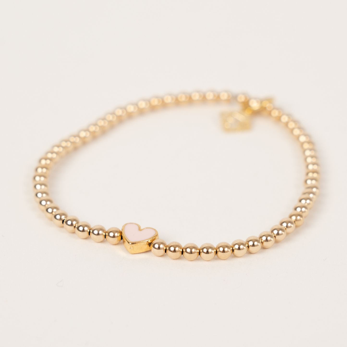 Gold beaded bracelet with a heart-shaped charm on a light background
