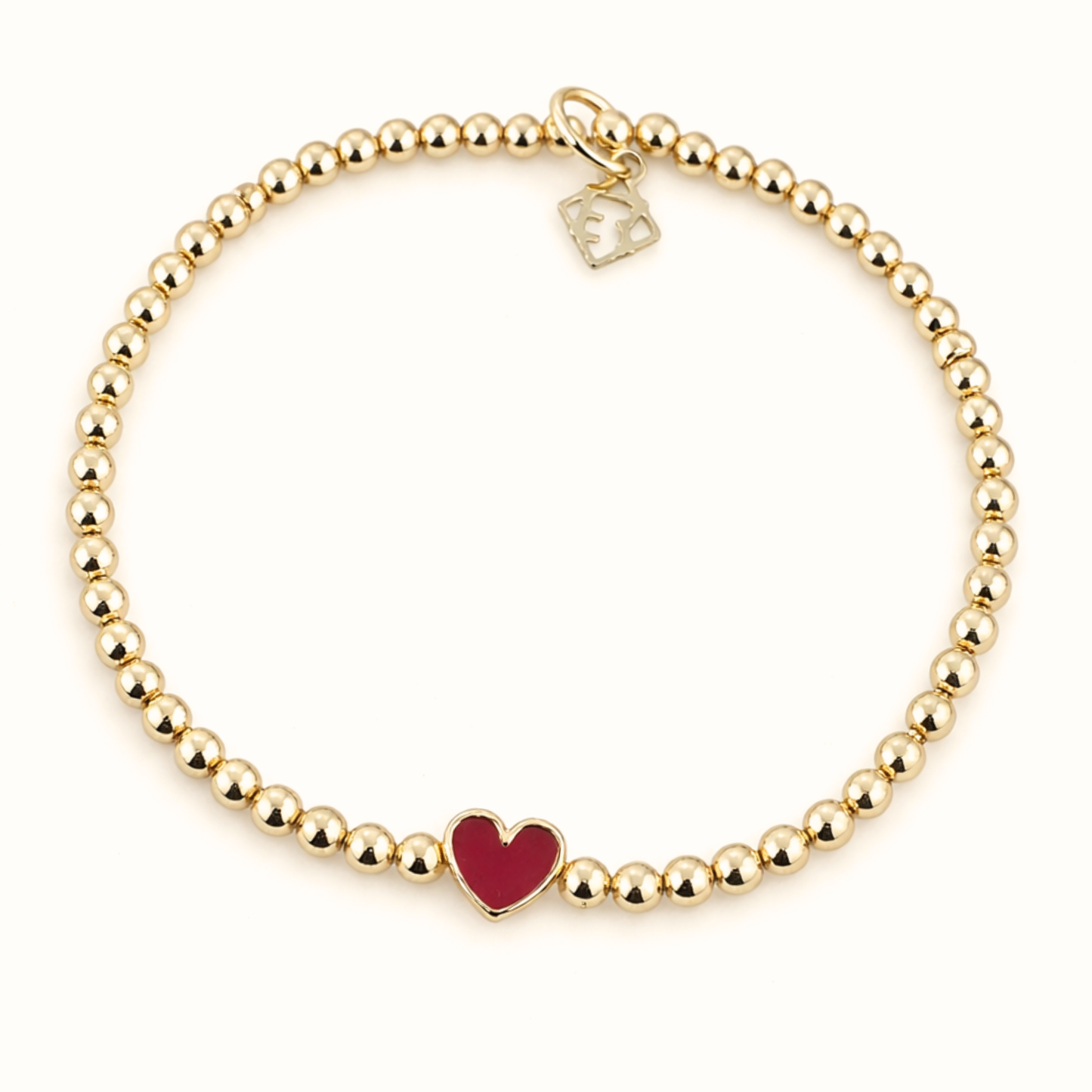 Gold beaded bracelet with a red heart charm on a white background