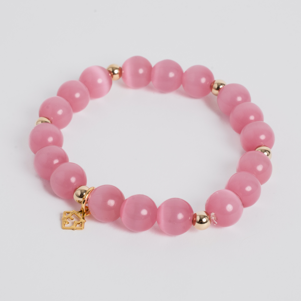 A pink beaded bracelet with polished round pink stones, small gold spacer beads, and a small gold charm, photographed on a clean light gray background.