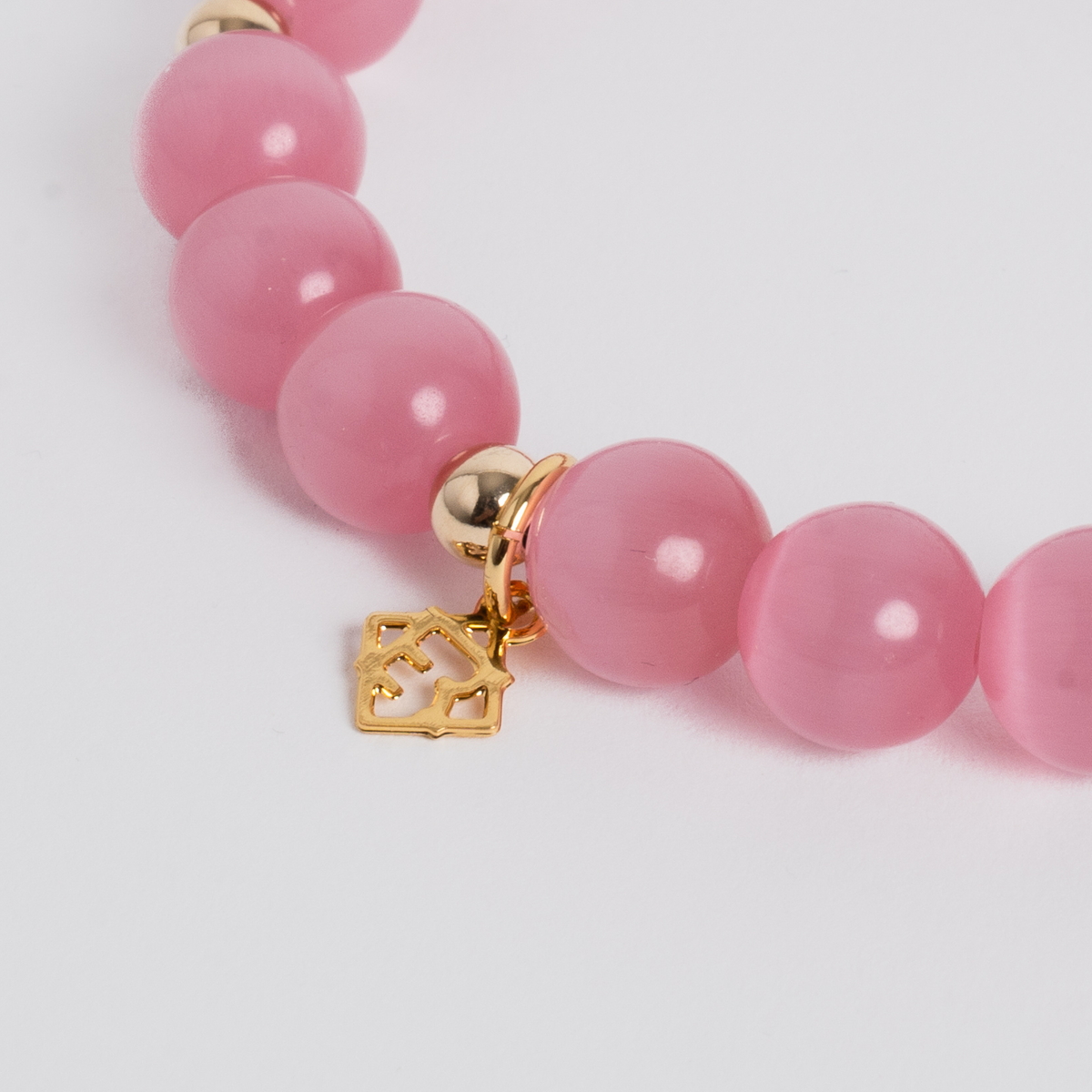 A close-up of a pink beaded bracelet with smooth round beads and a small gold-tone house-shaped charm, shown on a clean light gray background.