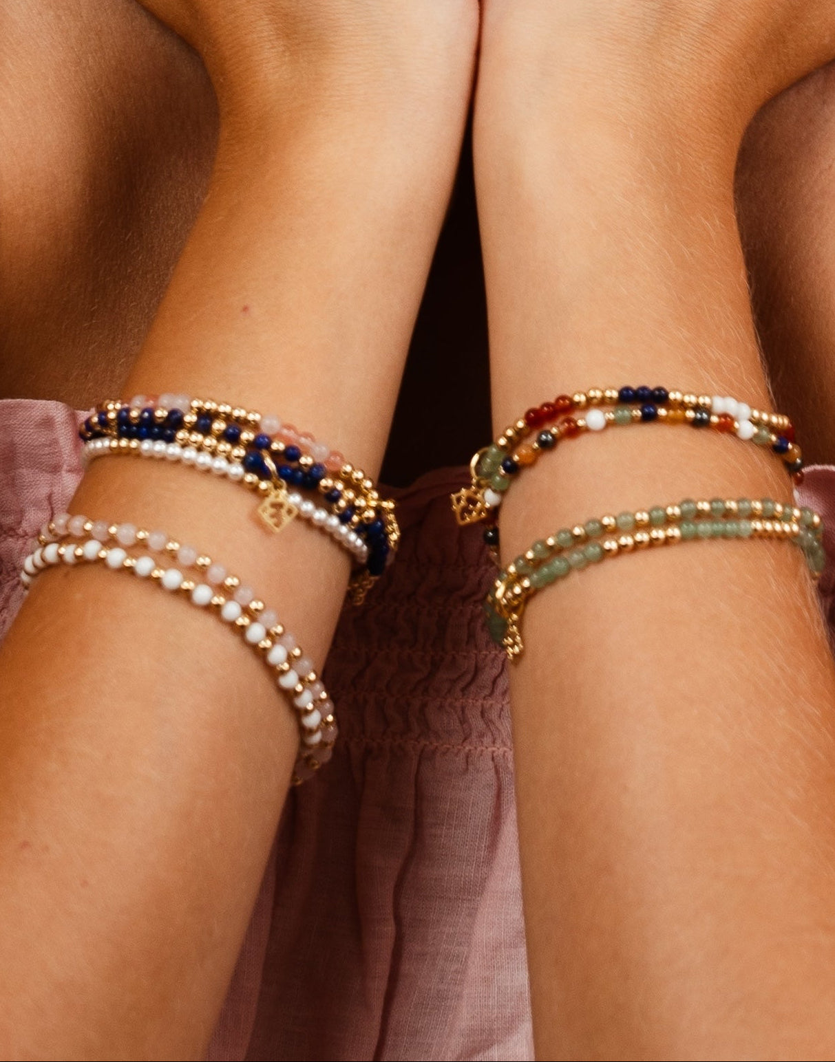 Two arms wearing beaded bracelets on a neutral background