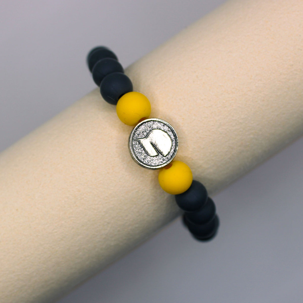 Close-up of the WIN bracelet’s pewter baseball hat bead between yellow and black silicone beads