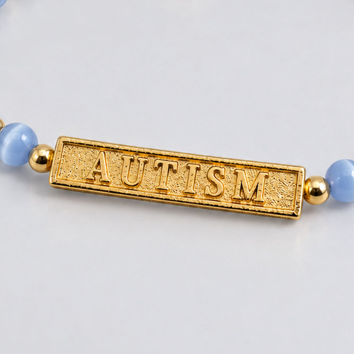 Close-up of the engraved gold AUTISM bar on a blue beaded bracelet