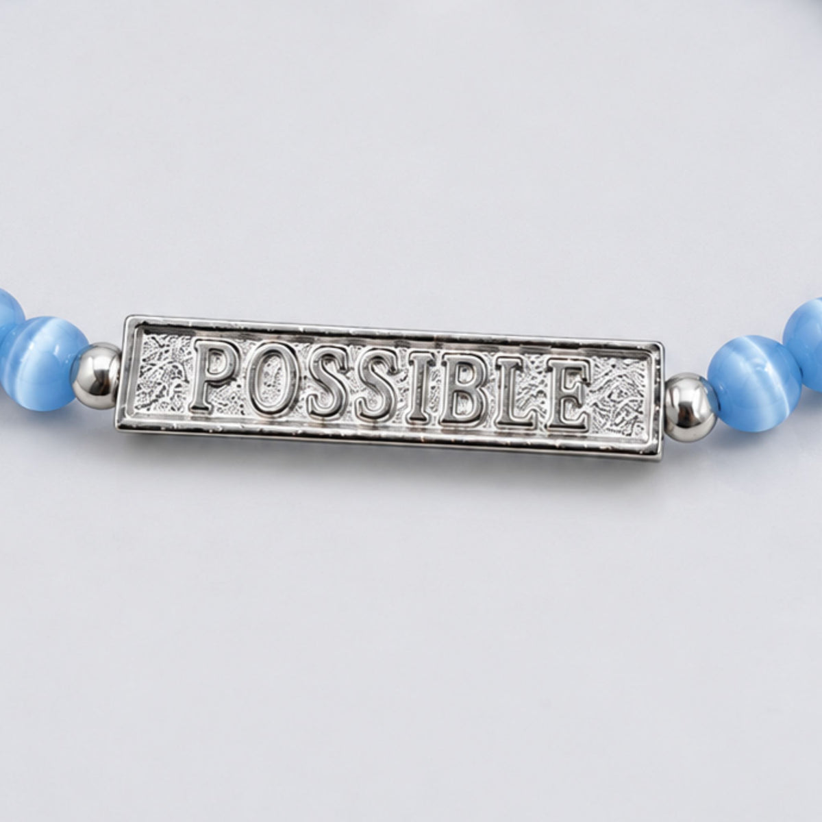Close-up of the engraved silver POSSIBLE bar on a blue beaded bracelet