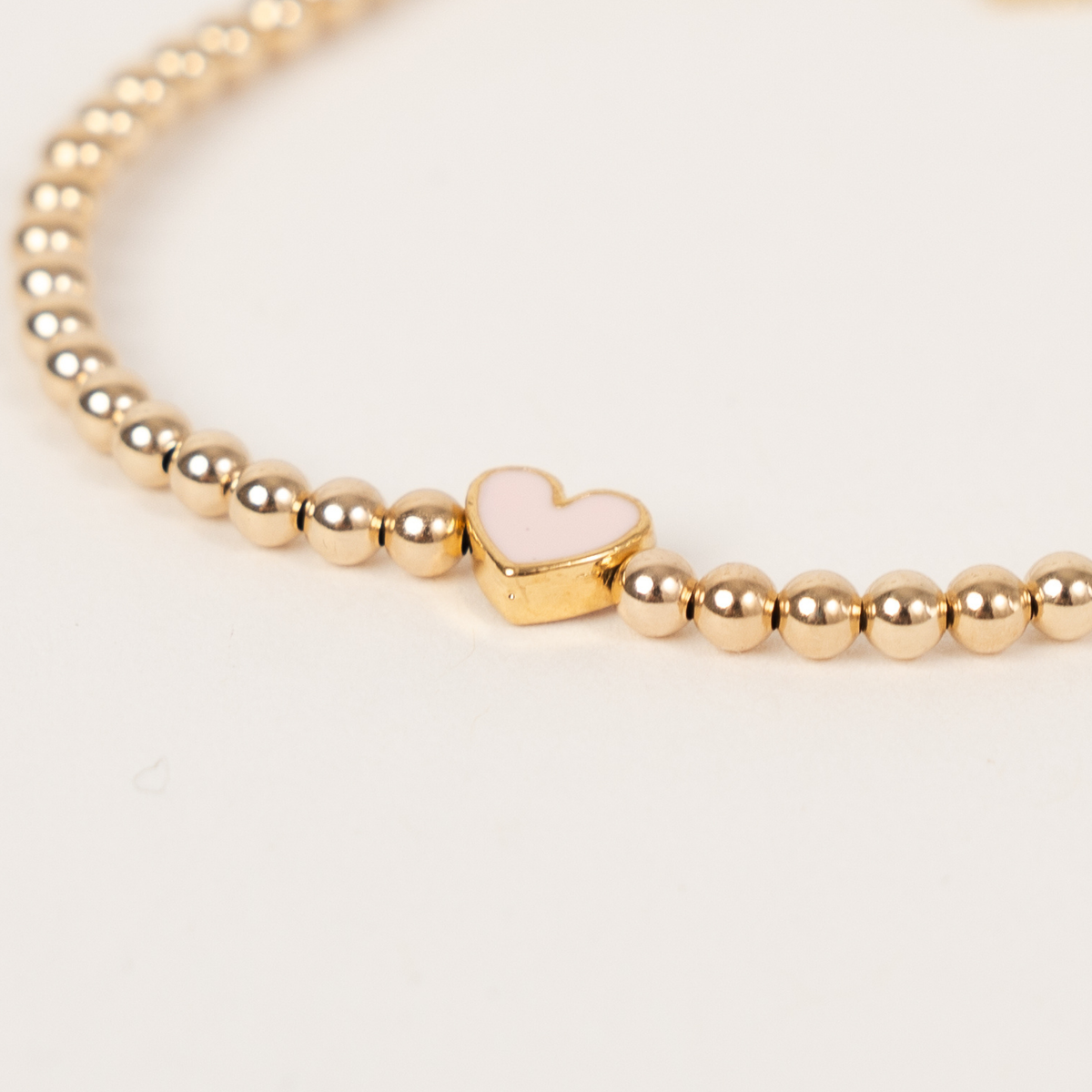 Close-up of the blush pink enamel heart and 3mm 14K gold-filled beads on the Blush Happy Heart Bracelet