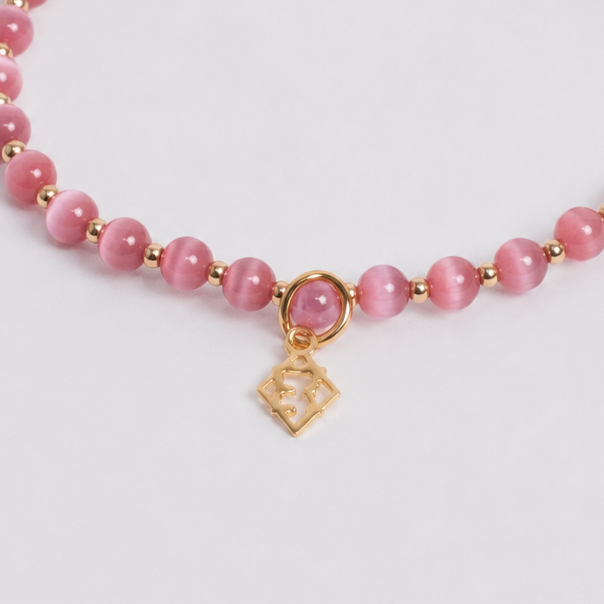 Close-up of dark pink cat’s-eye stones with 14K gold-filled beads and a golden ER charm