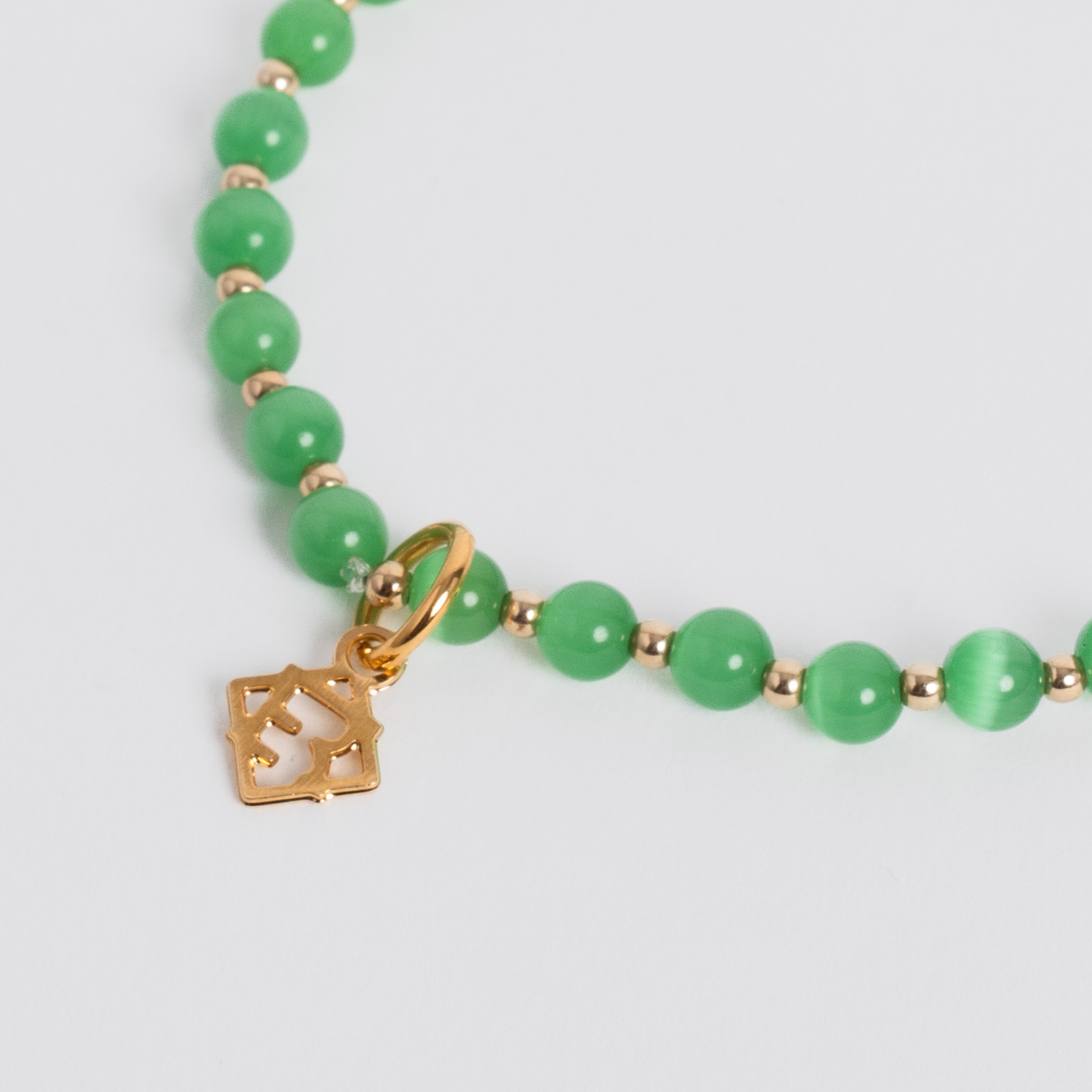 Close-up of deep green cat’s-eye stones with 14K gold-filled beads and a golden ER charm