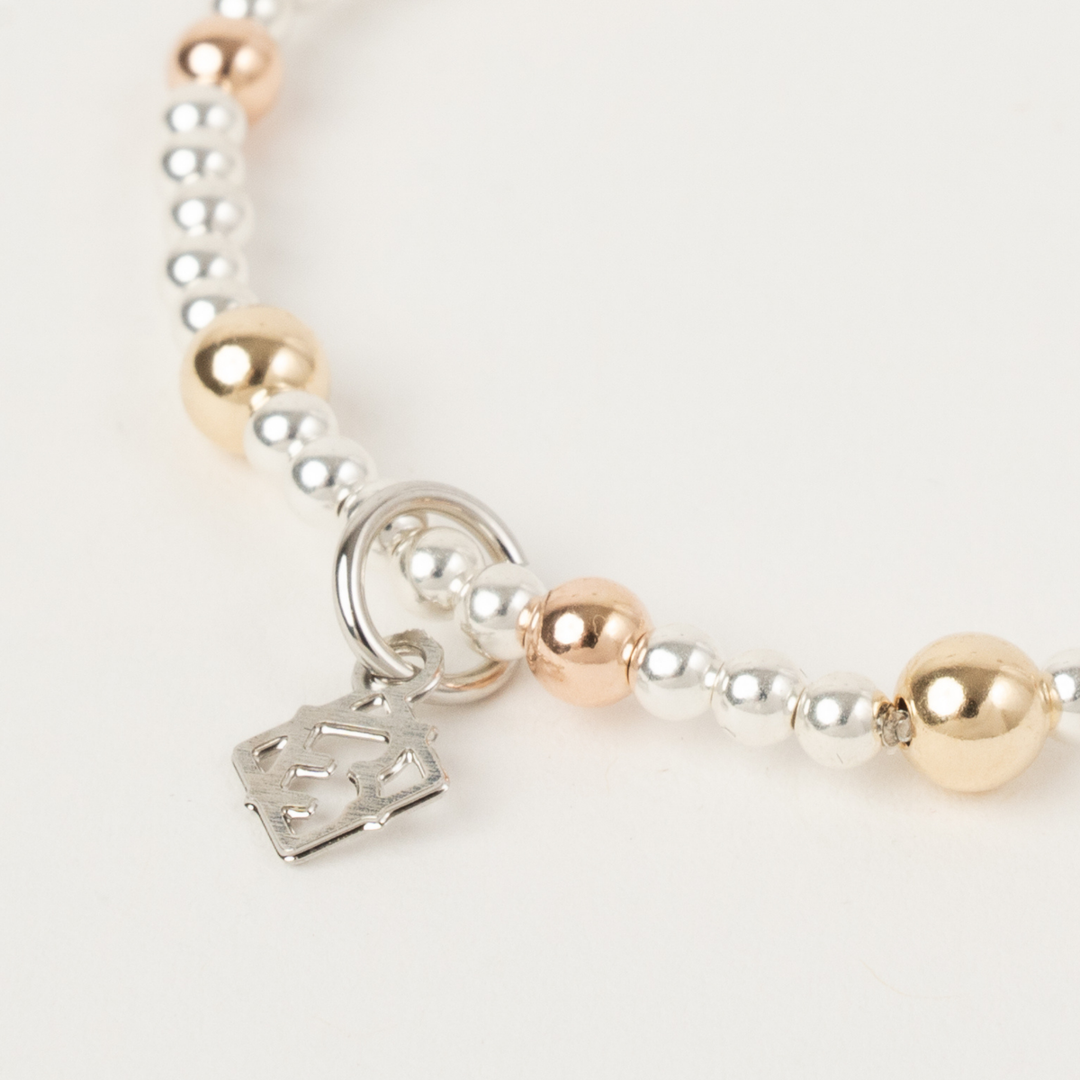 Close-up of the Lennon Blend Bracelet showing silver, gold and rose gold beads beside an ElyseRyan charm