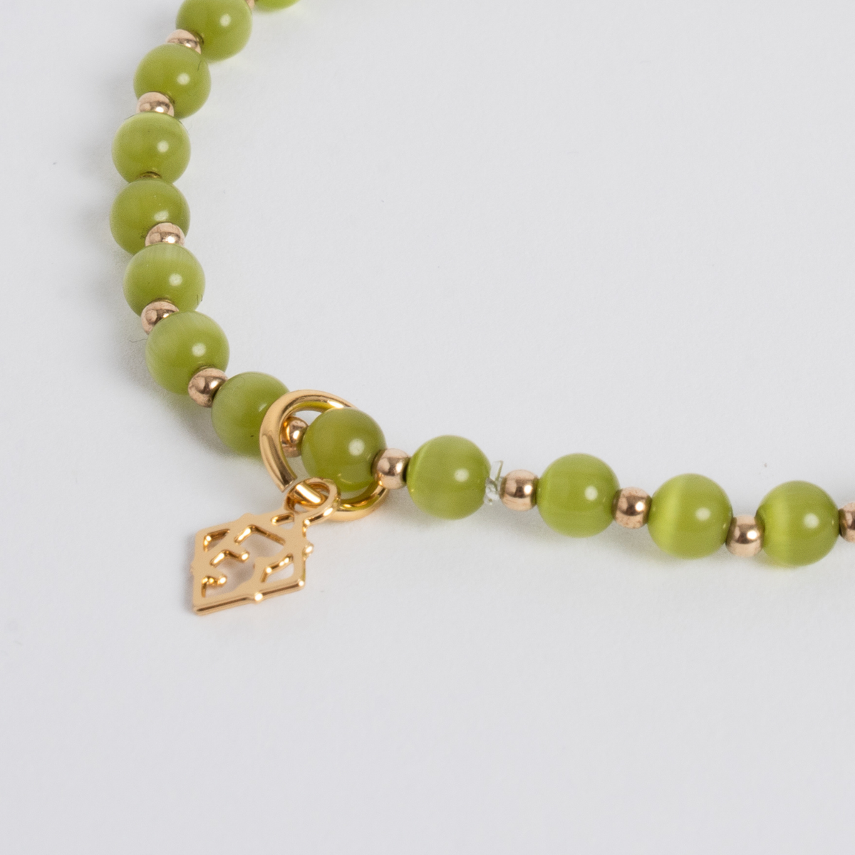 Close-up of lime green cat’s-eye stones with 14K gold-filled beads and a golden ER charm