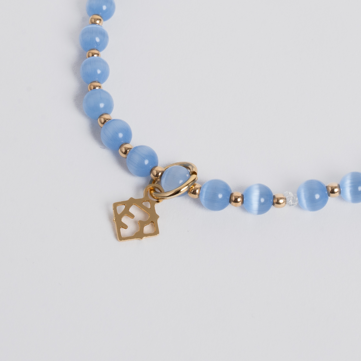 Close-up of ocean blue cat’s-eye stones with 14K gold-filled beads and a golden ER charm