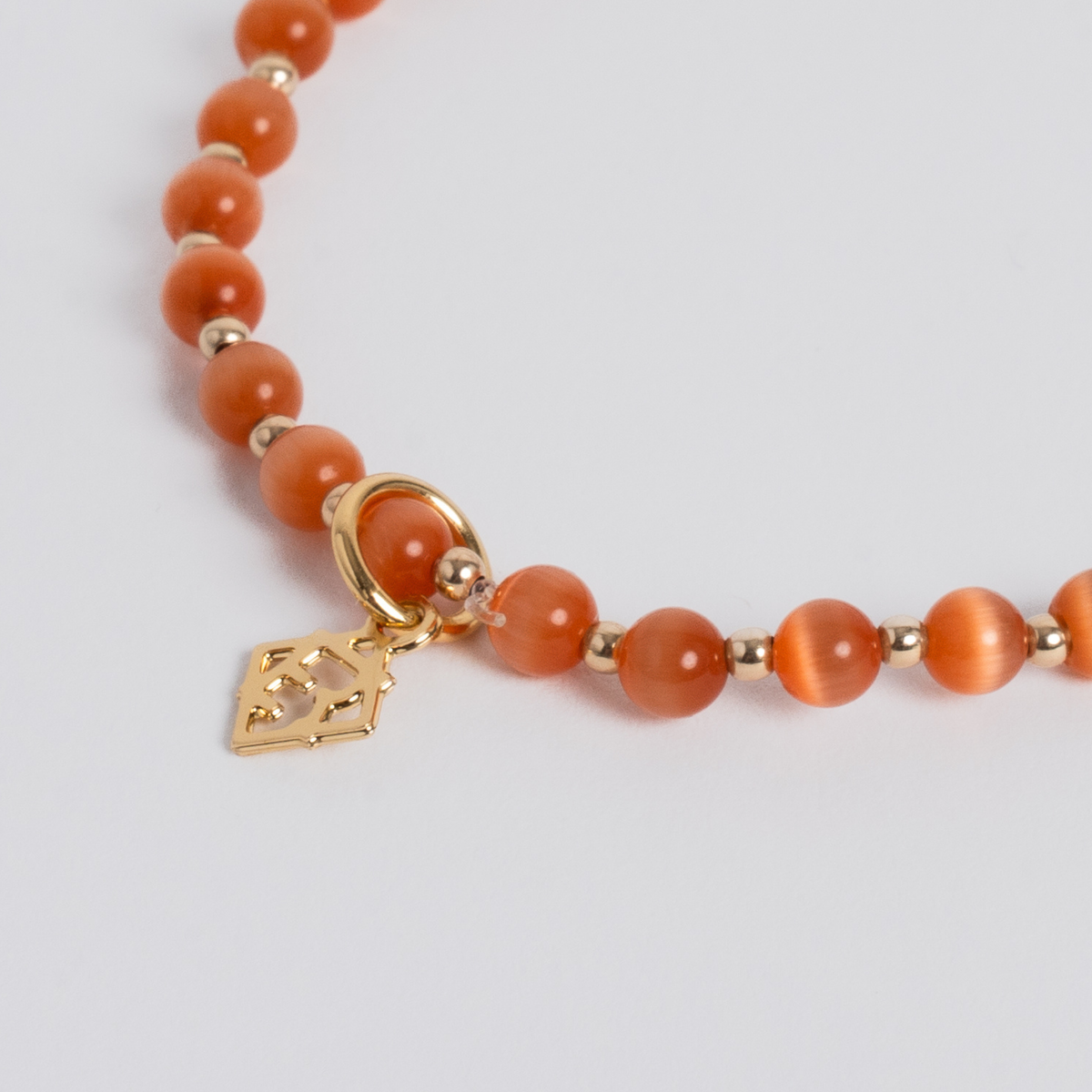 Close-up of orange cat’s-eye stones with 14K gold-filled beads and a golden ER charm