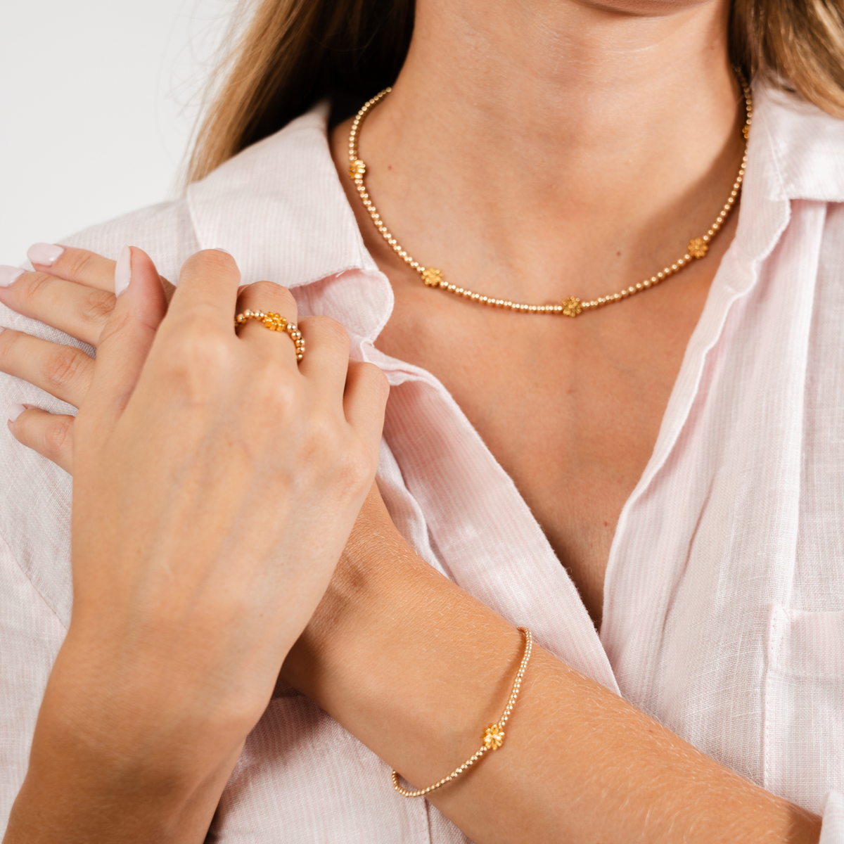 Woman wearing the 14K gold-filled Petite Fleur necklace, bracelet and ring with golden flower accents