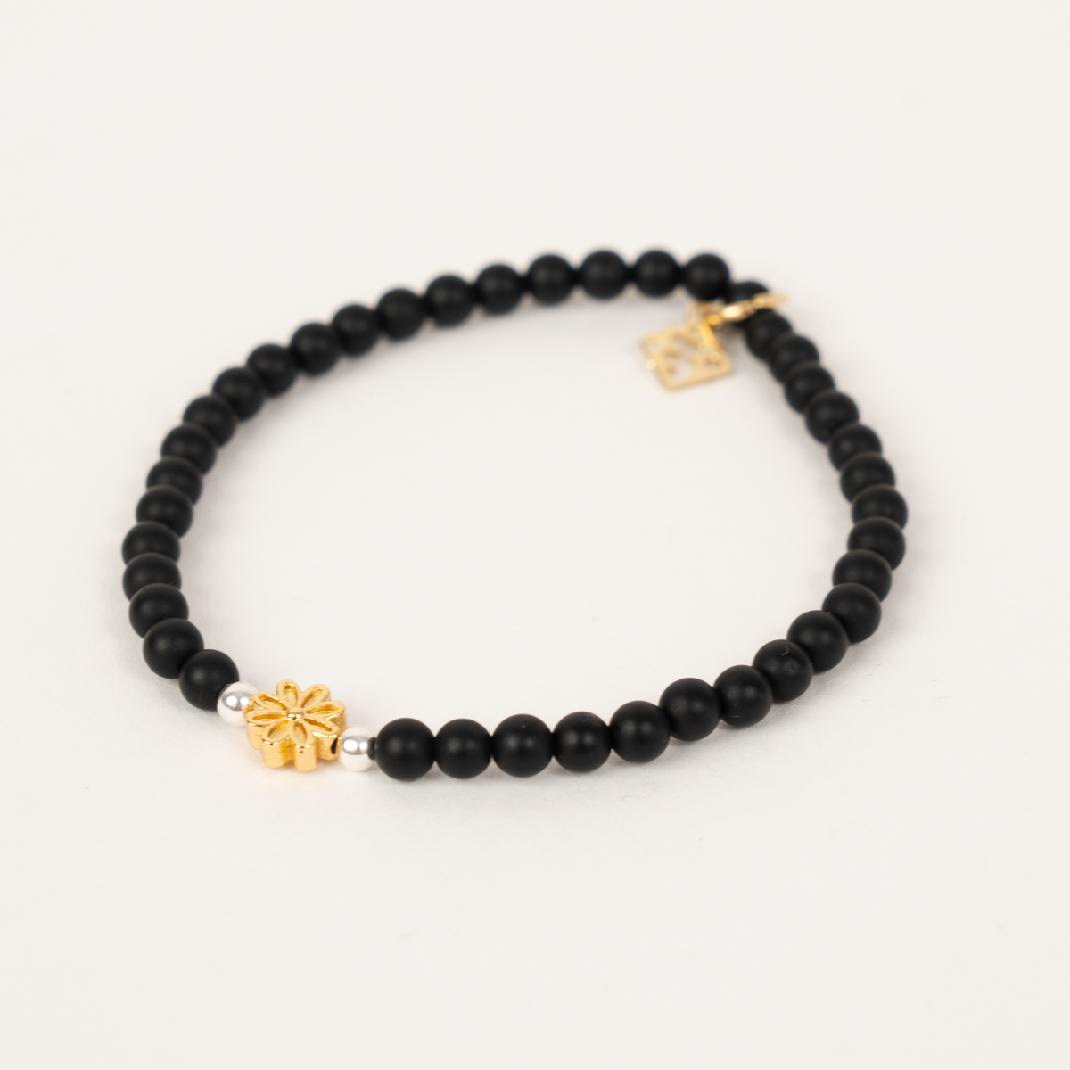 Petite Fleur bracelet with matte black beads, silver accents, a golden flower centerpiece and signature ER charm