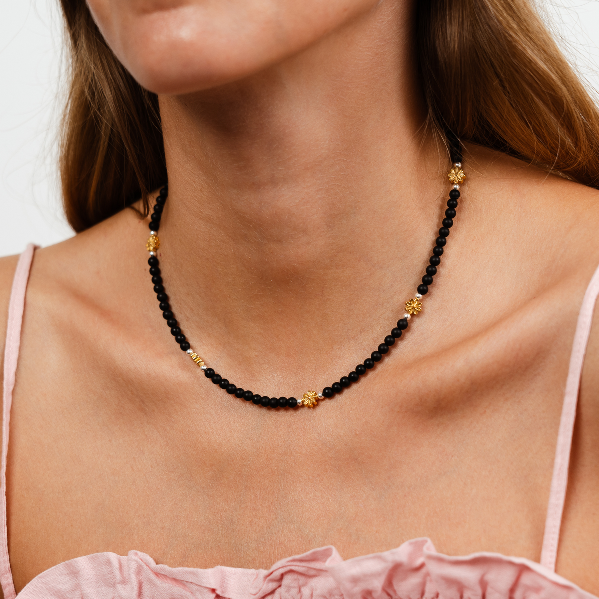 Woman wearing the Petite Fleur Necklace with 4mm matte black beads, silver-filled accents and five golden flowers